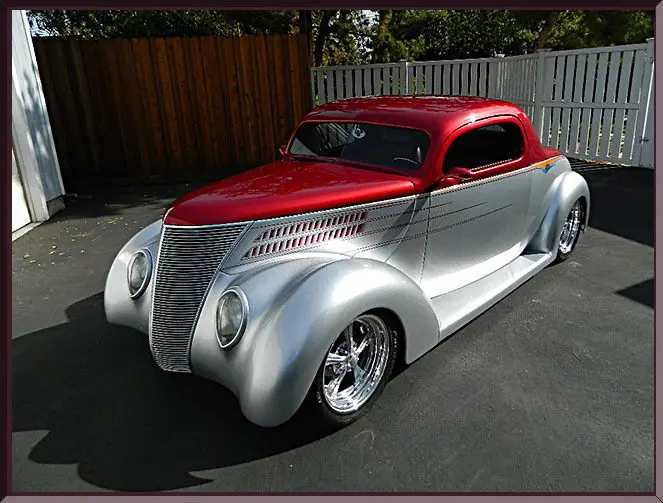 A shiny red and silver classic custom car parked outdoors.