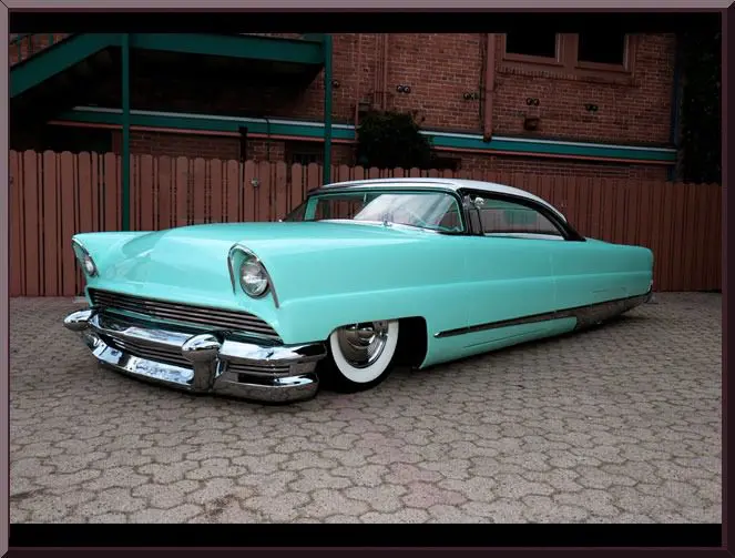 Classic turquoise vintage car parked on a cobblestone driveway at night.