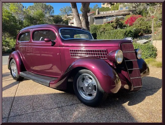 A vintage maroon classic car parked outdoors on a sunny day.