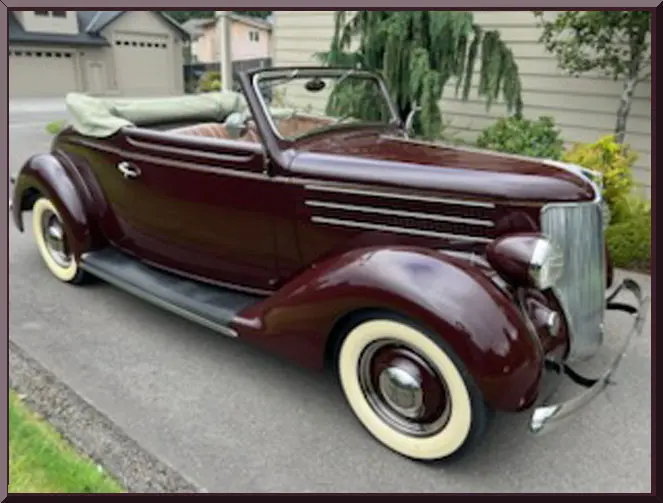A classic maroon convertible vintage car with whitewall tires parked outdoors.