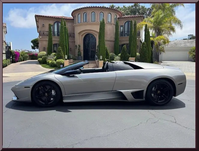 Silver convertible sports car in front of mansion.