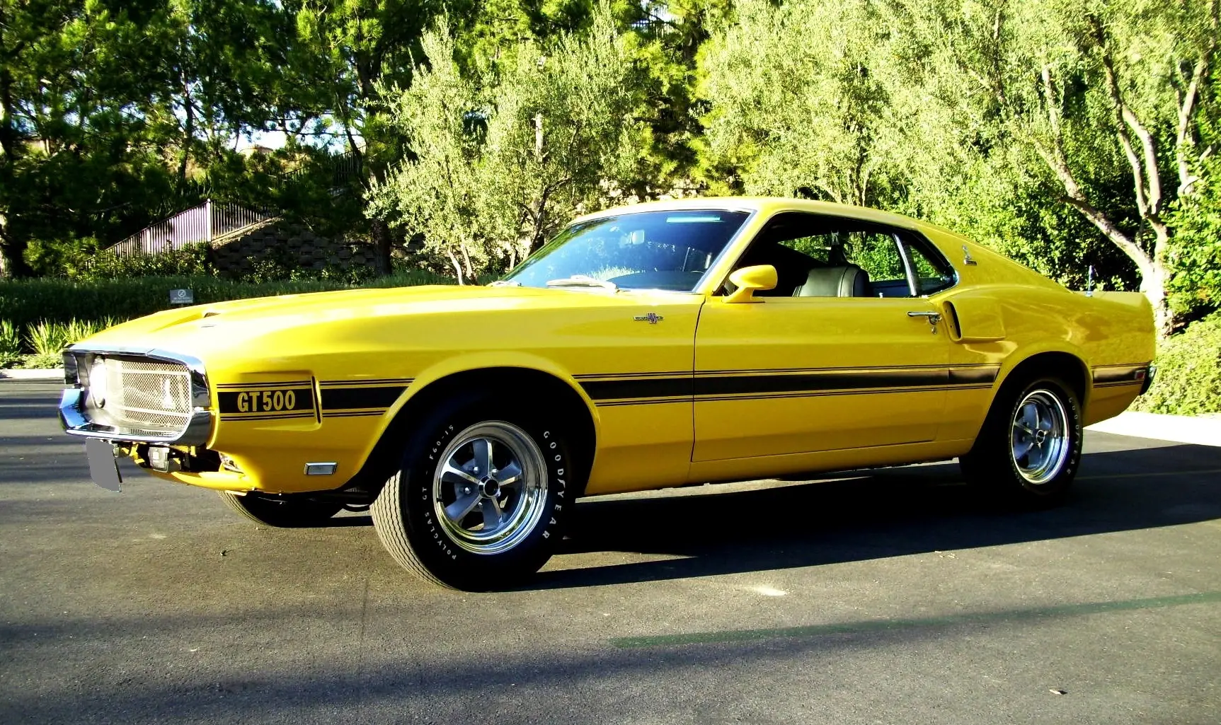 Yellow classic muscle car parked on a street with greenery.