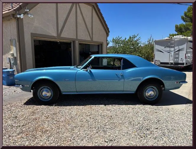 Classic blue convertible car parked outside a house on a sunny day.