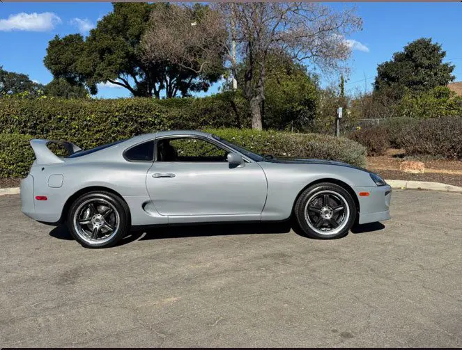 Silver sports car parked on a sunny day with green trees in the background.