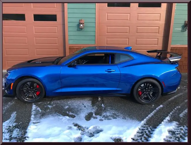 Blue sports car parked on snowy driveway.